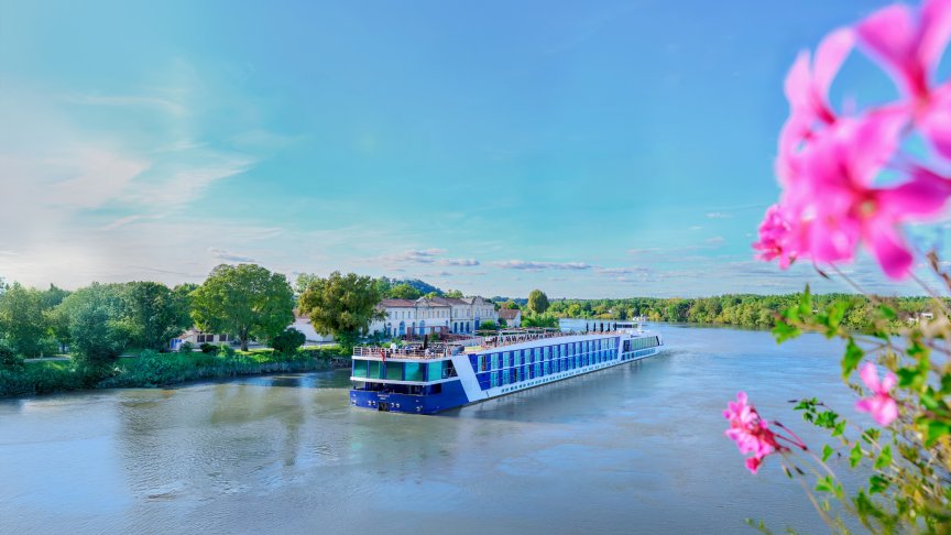 AmaWaterways’ AmaDolce river ship gliding along the Dordogne River in France, surrounded by lush countryside and golden afternoon light.