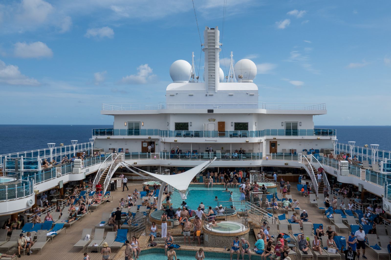 A lively cruise ship pool deck full of guests on a sunny day at sea