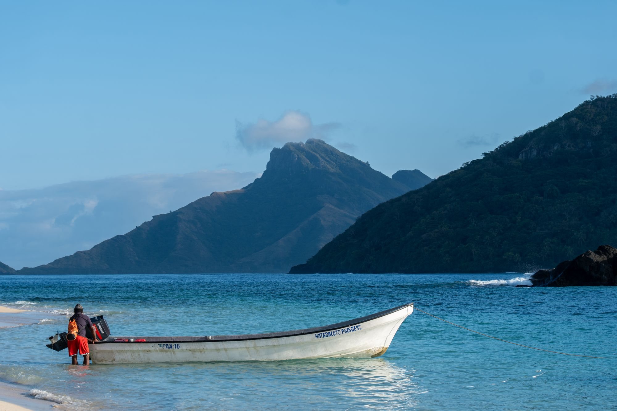 A peaceful scene of a boat by a beach against Fiji's stunning mountainous backdrop.
