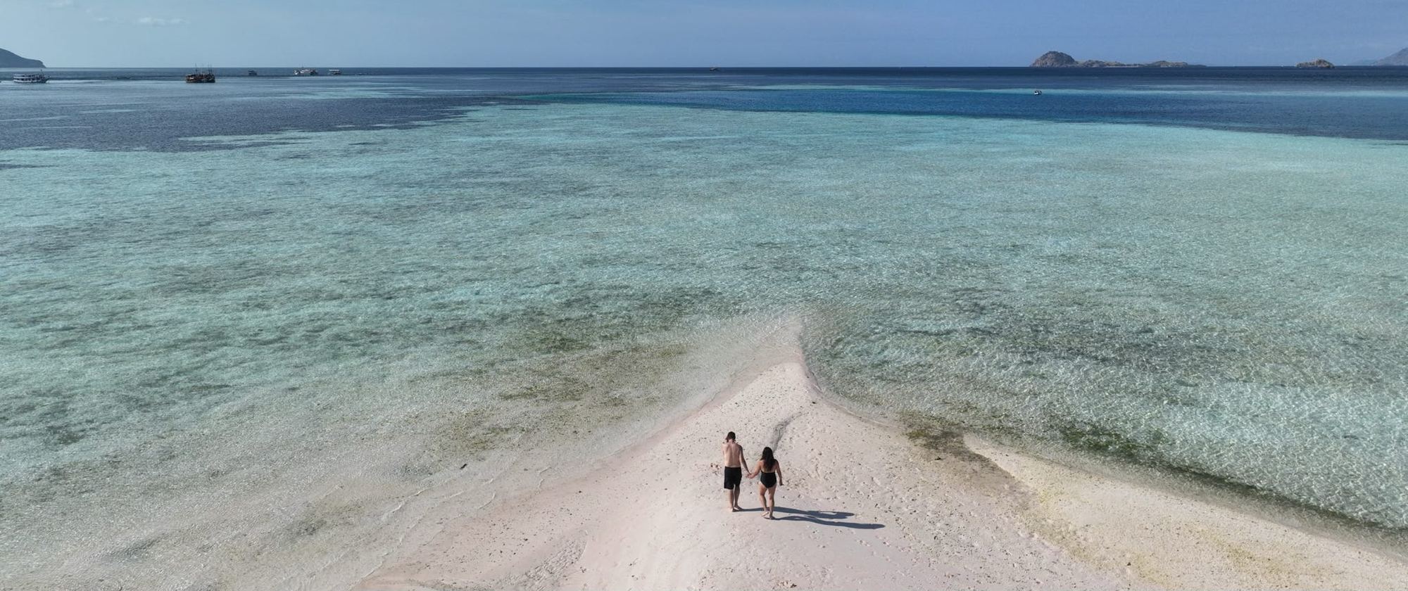 Two travelers walking a white sandbar into turquoise water