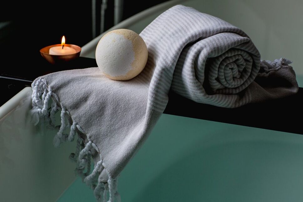 a towel and bath bomb sit on the edge of a tub to help welcome travelers home