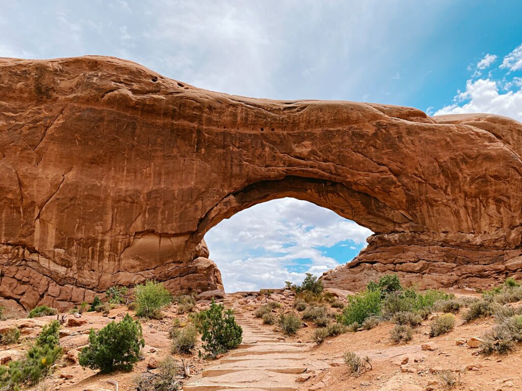 A large Arch at Arches National Park in Utah shows a blue and cloudy sky though the arch