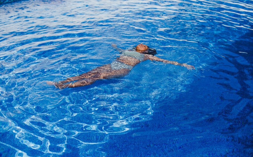 a woman lays face up in a swimming pool on a sunny day with her eyes closed