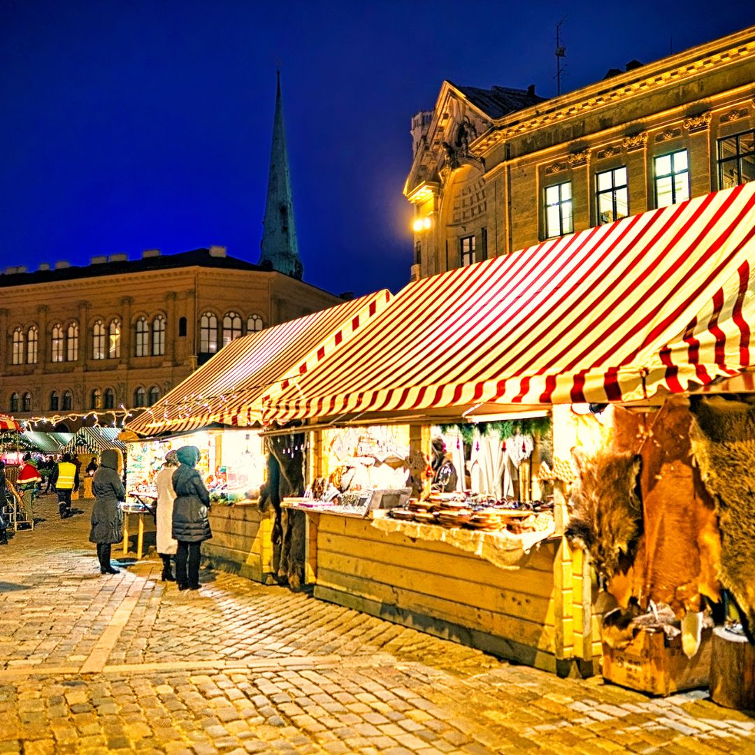 Traditional European Christmas market with striped tents and historic buildings at dusk.