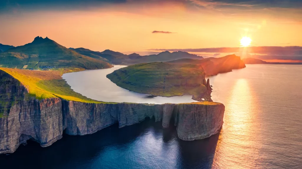 Aerial view of the sun setting over the breathtaking cliffs and calm waters of the Faroe Islands, Denmark.